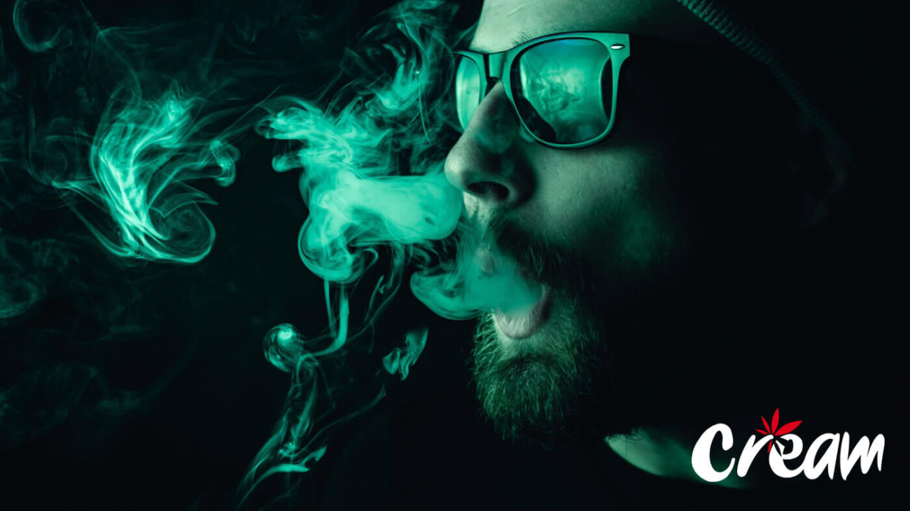 Man exhaling smoke with a green overlay at CREAM cannabis dispensary in Jersey City.