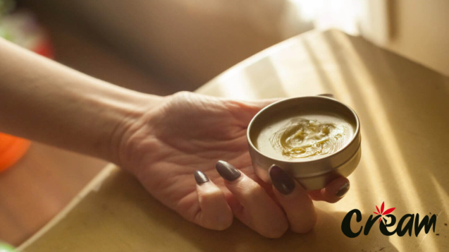 Hand holding cannabis salve in a container at CREAM cannabis dispensary in Jersey City.